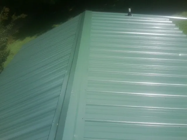 New green metal panels meeting at the ridge of a roof — Flat Roof Repair work by our crew in La Grange